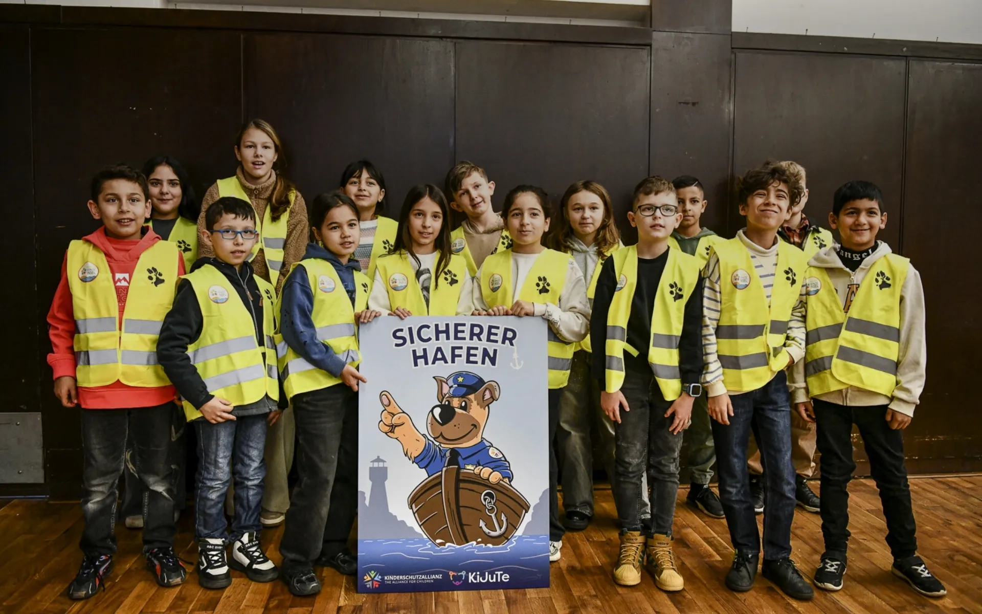 Kinder in gelben Warnwesten halten ein Plakat Sicherer Hafen mit Basko